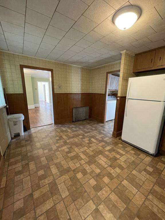 unfurnished room with washer / dryer, radiator, brick patterned flooring, a wainscoted wall, and wood walls
