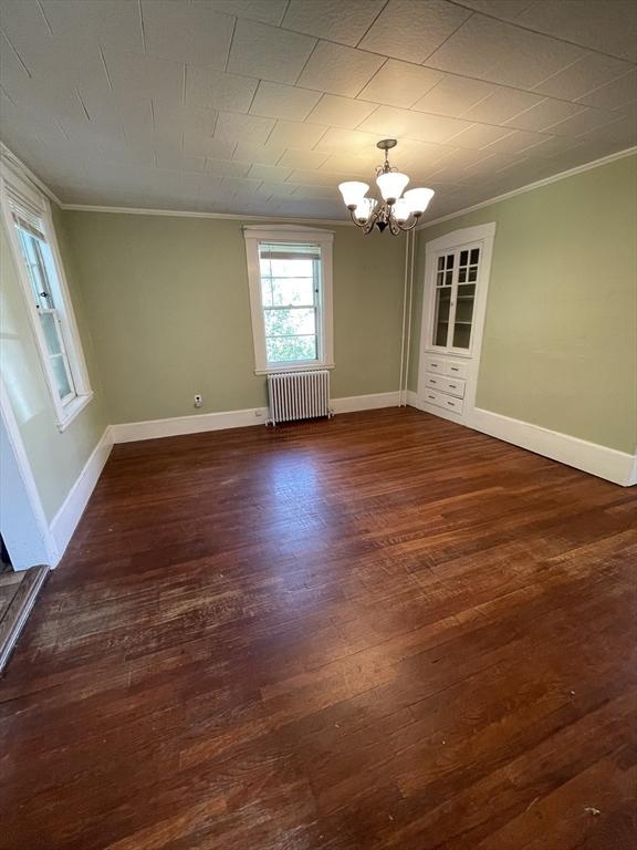 unfurnished dining area with radiator, crown molding, a chandelier, wood finished floors, and baseboards