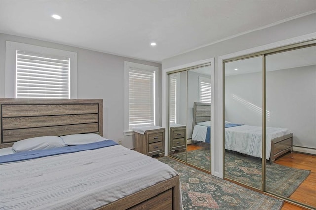 bedroom featuring a baseboard radiator, hardwood / wood-style floors, and two closets