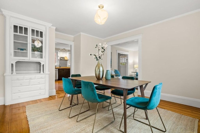 dining area with light wood-style floors, baseboards, and crown molding