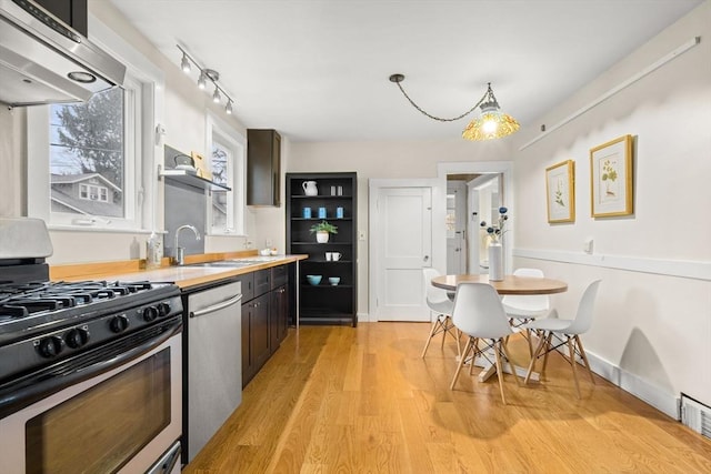 kitchen featuring appliances with stainless steel finishes, range hood, open shelves, a sink, and light wood finished floors