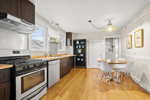 kitchen featuring dark brown cabinetry, a sink, light countertops, stainless steel appliances, and under cabinet range hood