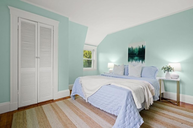 bedroom with a closet, baseboards, vaulted ceiling, and wood finished floors