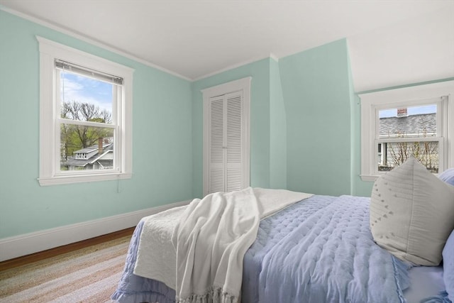bedroom with baseboards, multiple windows, ornamental molding, and wood finished floors