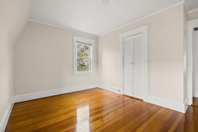 unfurnished bedroom with baseboards, ornamental molding, a closet, and hardwood / wood-style flooring