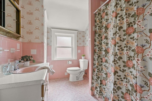 full bathroom featuring tile patterned flooring, vanity, toilet, tile walls, and a wainscoted wall
