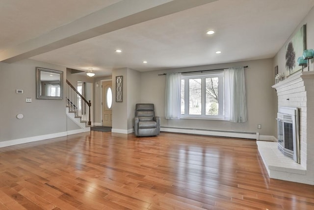 unfurnished living room with stairway, light wood-style floors, a fireplace, baseboards, and baseboard heating