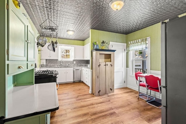 kitchen with light wood-type flooring, backsplash, stainless steel appliances, sink, and white cabinetry