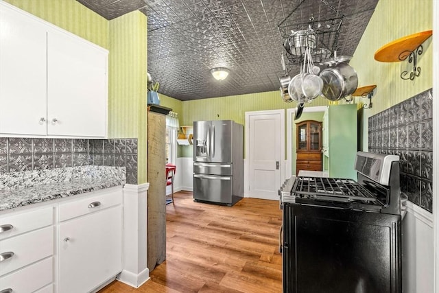 kitchen with backsplash, black range with gas stovetop, white cabinets, stainless steel fridge with ice dispenser, and light hardwood / wood-style floors