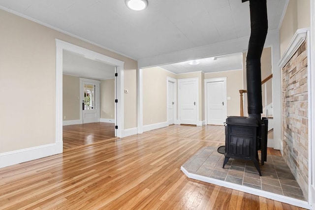 unfurnished living room with light wood-type flooring, baseboards, ornamental molding, and a wood stove