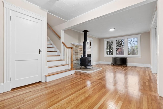 unfurnished living room featuring hardwood / wood-style flooring, radiator, ornamental molding, and a wood stove