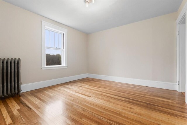 empty room with radiator, light wood-style flooring, and baseboards