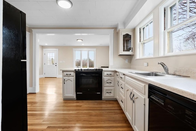 kitchen with black appliances, a sink, light countertops, and light wood-style floors