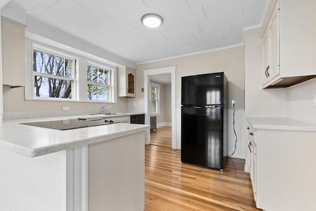 kitchen featuring light wood-type flooring, crown molding, black appliances, a peninsula, and white cabinetry