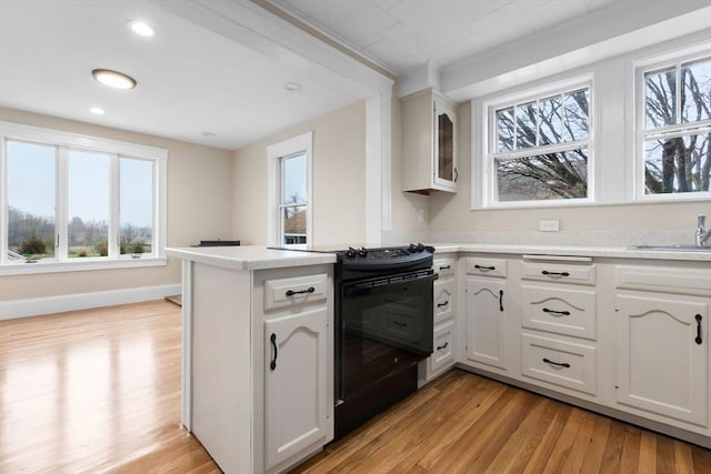 kitchen featuring plenty of natural light, a peninsula, black electric range, and light wood-style flooring