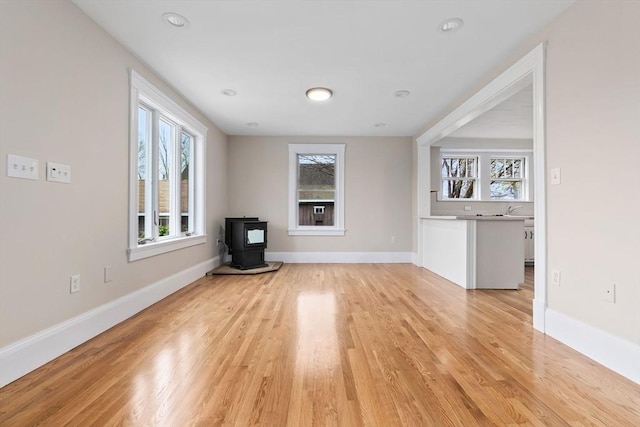 unfurnished living room with light wood-type flooring, a wood stove, baseboards, and a healthy amount of sunlight