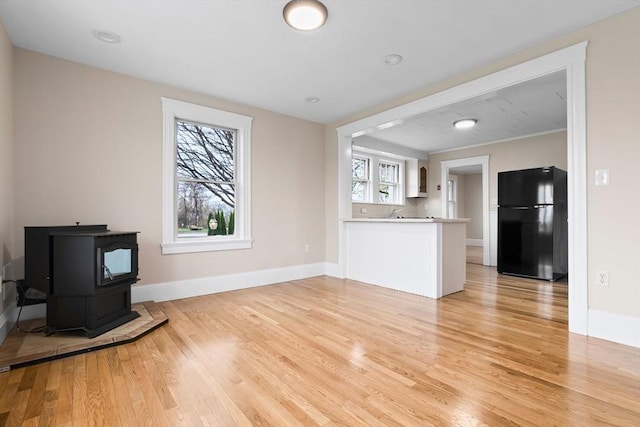 unfurnished living room with light wood-style flooring, baseboards, and a wood stove