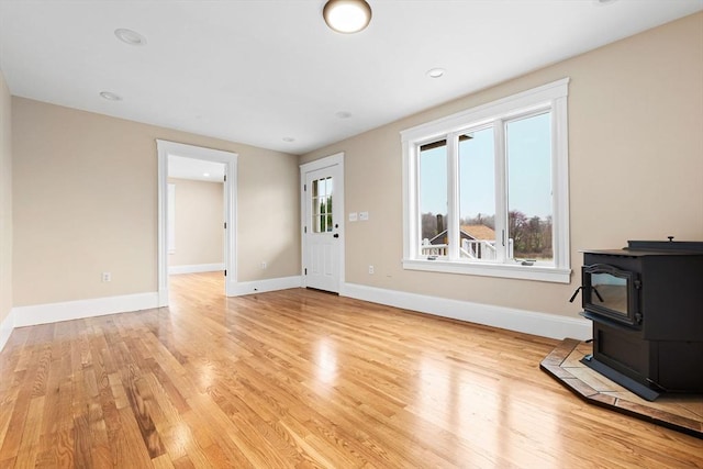 unfurnished living room with light wood-style flooring, a wood stove, and baseboards