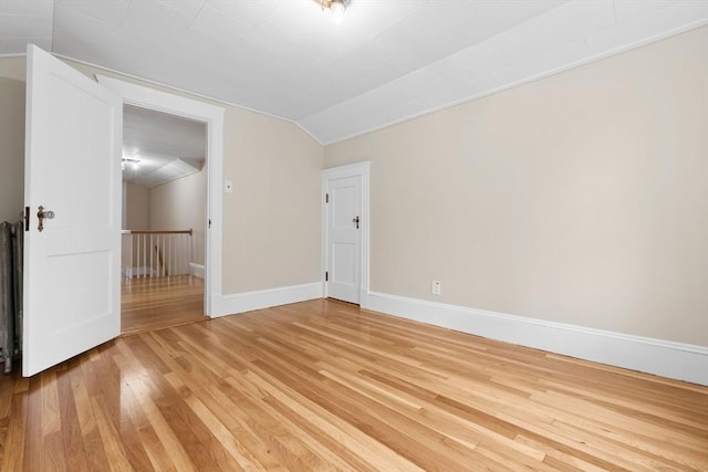 unfurnished room featuring vaulted ceiling, light wood-style floors, and baseboards