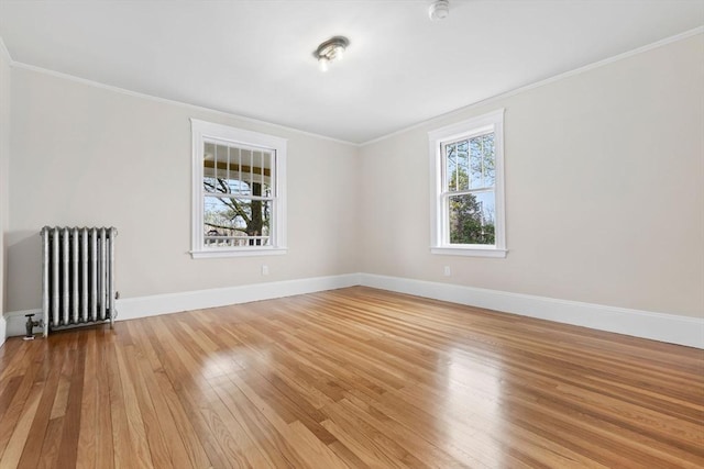 empty room with radiator, light wood-style floors, baseboards, and ornamental molding