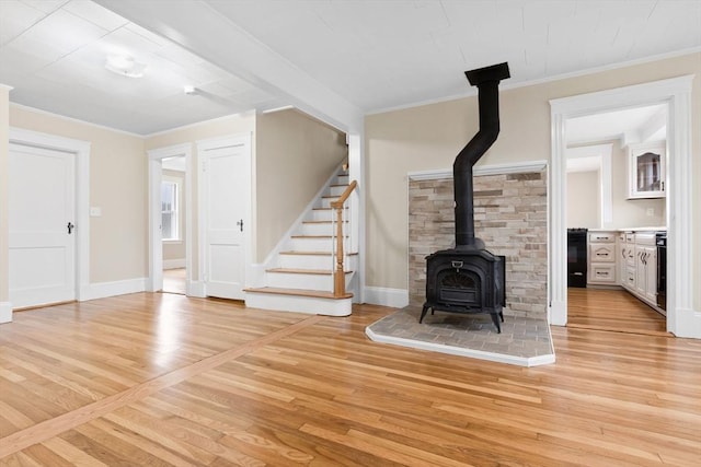 unfurnished living room featuring ornamental molding, a wood stove, stairs, and light wood-style flooring