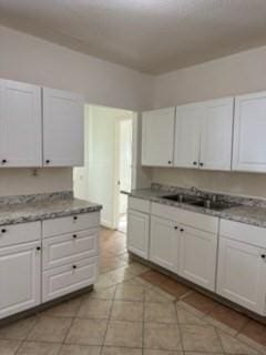 kitchen featuring light tile patterned flooring, light stone counters, white cabinetry, and sink