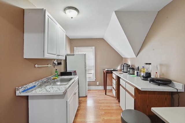 kitchen featuring sink, light hardwood / wood-style flooring, white refrigerator, lofted ceiling, and white cabinets