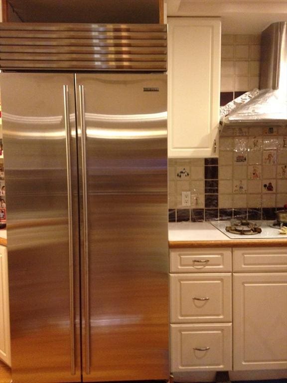 12 Inis Cir, Newton, MA 02465 - kitchen with built in fridge, white cabinets, wall chimney exhaust hood, decorative backsplash, and light countertops