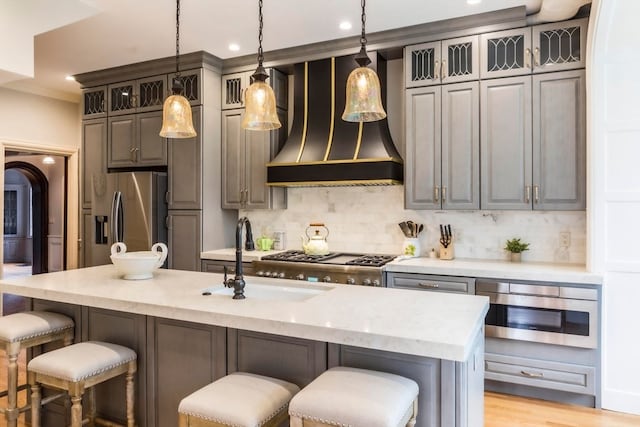 kitchen with sink, light wood-type flooring, stainless steel fridge, premium range hood, and a kitchen island with sink