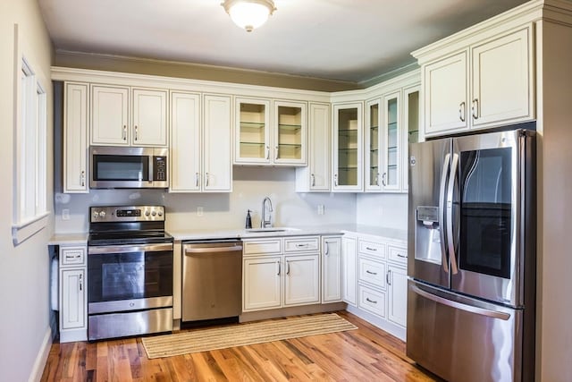 kitchen with appliances with stainless steel finishes, light hardwood / wood-style flooring, sink, and white cabinetry