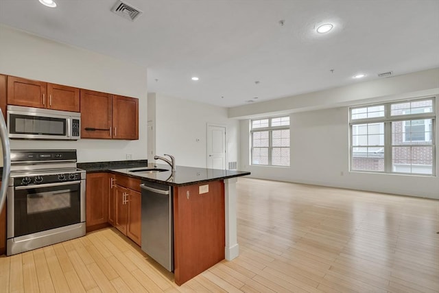 kitchen with sink, light hardwood / wood-style flooring, stainless steel appliances, and dark stone countertops