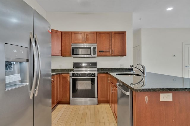 kitchen featuring stainless steel appliances, dark stone countertops, sink, kitchen peninsula, and light hardwood / wood-style flooring