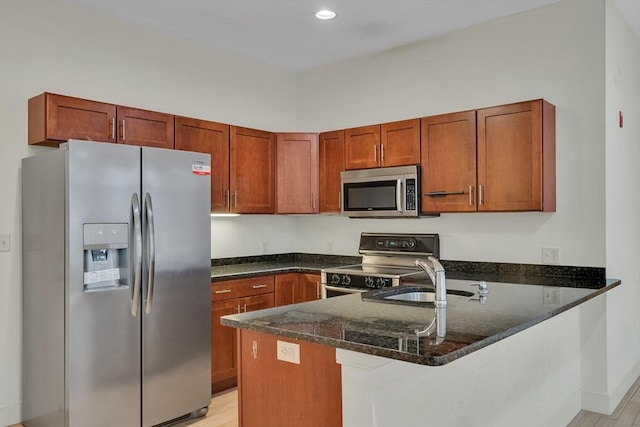 kitchen featuring a kitchen bar, sink, dark stone countertops, kitchen peninsula, and stainless steel appliances