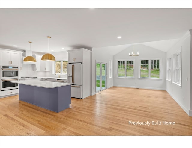 kitchen featuring vaulted ceiling, high end white refrigerator, pendant lighting, a center island, and white cabinetry