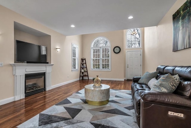 living room featuring a glass covered fireplace, recessed lighting, baseboards, and wood finished floors