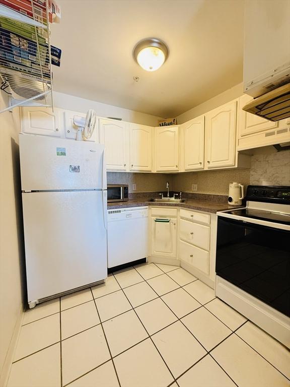 kitchen with dark countertops, white appliances, range hood, white cabinets, and a sink