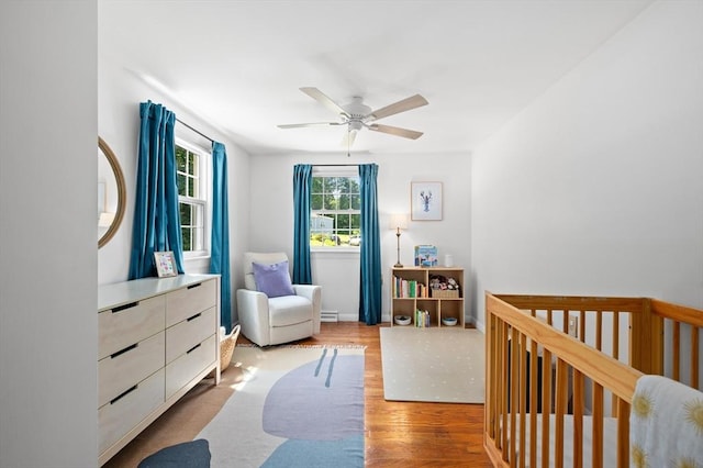 241 W Main St, Westborough, MA 01581 - bedroom featuring wood finished floors, a crib, baseboard heating, and ceiling fan