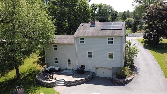 241 W Main St, Westborough, MA 01581 - back of property with asphalt driveway, solar panels, a chimney, a patio, and an attached garage