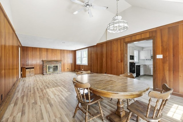 dining room with ceiling fan with notable chandelier, lofted ceiling, a fireplace, and wooden walls