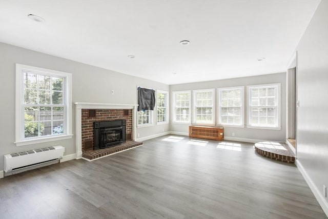 unfurnished living room with a baseboard heating unit, a brick fireplace, wood-type flooring, and radiator heating unit