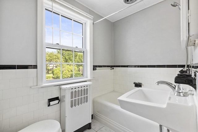 full bathroom with radiator, tile walls, plenty of natural light, and sink