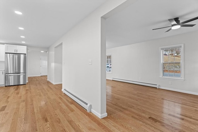 unfurnished living room with light wood-type flooring, ceiling fan, and a baseboard heating unit