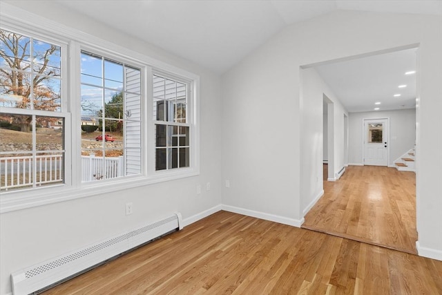 empty room featuring light wood-type flooring, vaulted ceiling, and a baseboard heating unit