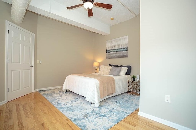 bedroom featuring ceiling fan, baseboards, beam ceiling, and light wood-style flooring