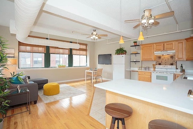 kitchen featuring under cabinet range hood, white appliances, light wood-style floors, a peninsula, and light countertops