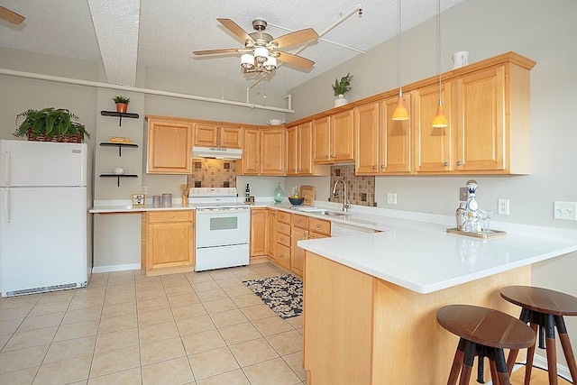 kitchen featuring light brown cabinets, under cabinet range hood, a peninsula, white appliances, and a sink