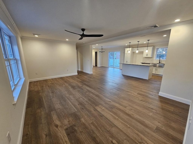 unfurnished living room with crown molding, dark wood-type flooring, ceiling fan with notable chandelier, and sink