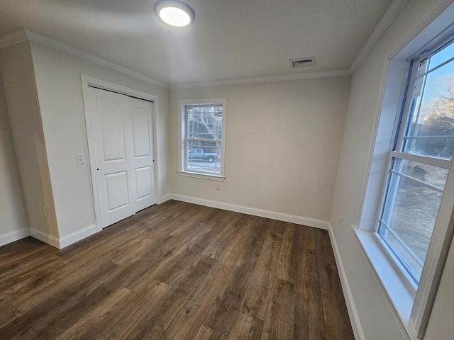 unfurnished bedroom featuring multiple windows, ornamental molding, dark hardwood / wood-style floors, and a closet