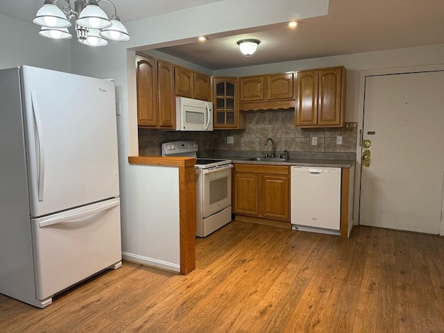 kitchen with light wood finished floors, tasteful backsplash, brown cabinetry, white appliances, and a sink