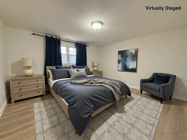 bedroom with baseboards, light wood-type flooring, and a textured ceiling